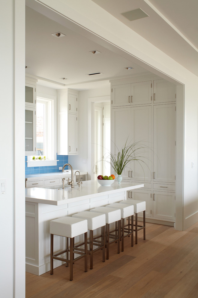 Photo of a beach style separate kitchen in New York with shaker cabinets, white cabinets, blue splashback, medium hardwood floors, with island and brown floor.
