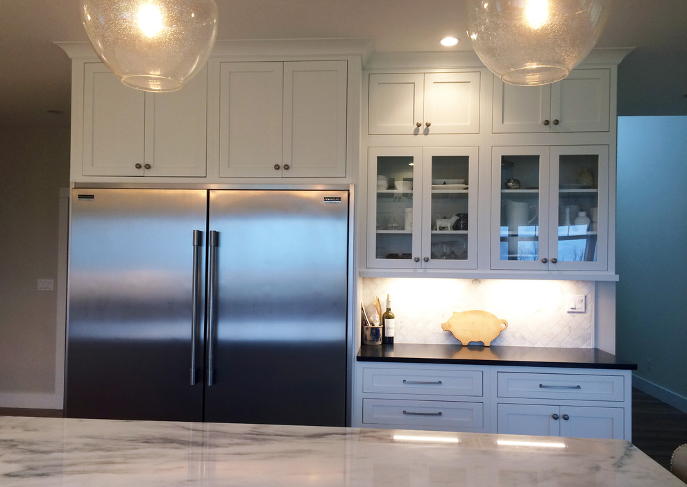 Kitchen pantry - large transitional l-shaped dark wood floor and brown floor kitchen pantry idea with a farmhouse sink, recessed-panel cabinets, white cabinets, quartz countertops, beige backsplash, ceramic backsplash, stainless steel appliances, an island and black countertops
