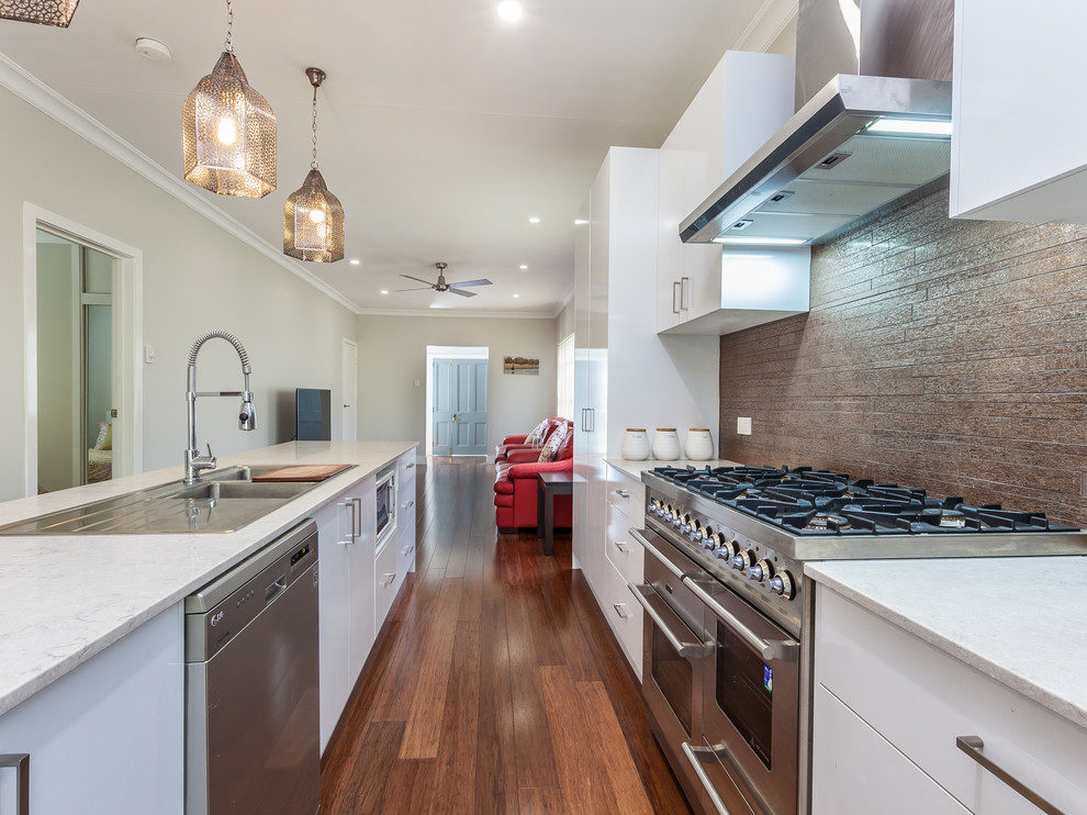 Mid-sized modern galley eat-in kitchen in Brisbane with a drop-in sink, white cabinets, quartz benchtops, metallic splashback, matchstick tile splashback, stainless steel appliances, bamboo floors and with island.