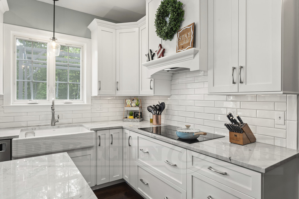 Design ideas for a large country l-shaped kitchen in Providence with a farmhouse sink, shaker cabinets, white cabinets, quartzite benchtops, white splashback, ceramic splashback, stainless steel appliances, dark hardwood floors, with island, brown floor and grey benchtop.