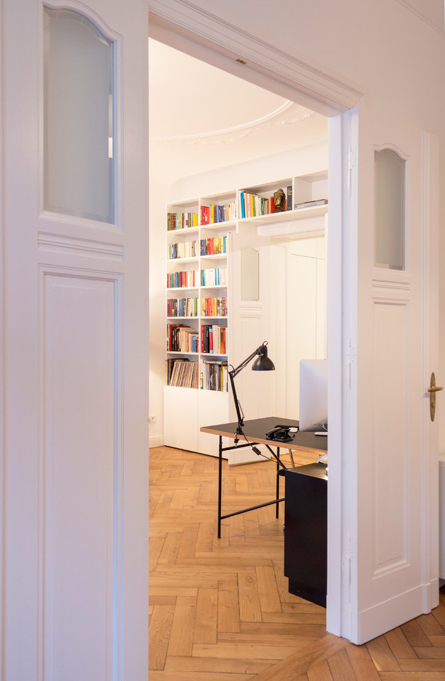 This is an example of an expansive contemporary home office in Berlin with a library, white walls, medium hardwood floors, no fireplace, a freestanding desk and beige floor.
