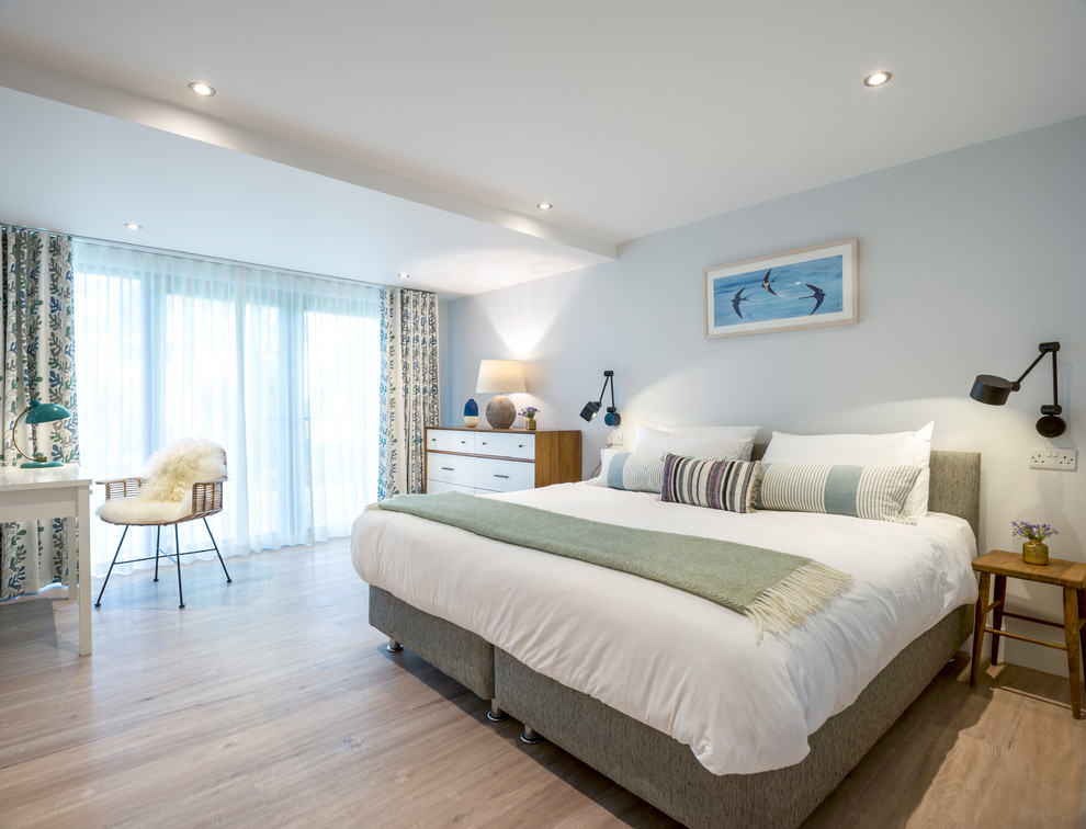 Photo of a large beach style master bedroom in Cornwall with grey walls, light hardwood floors and beige floor.