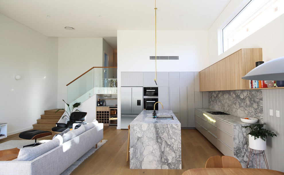 This is an example of a contemporary l-shaped open plan kitchen in Sydney with an undermount sink, flat-panel cabinets, grey cabinets, grey splashback, stone slab splashback, medium hardwood floors, with island, brown floor and grey benchtop.