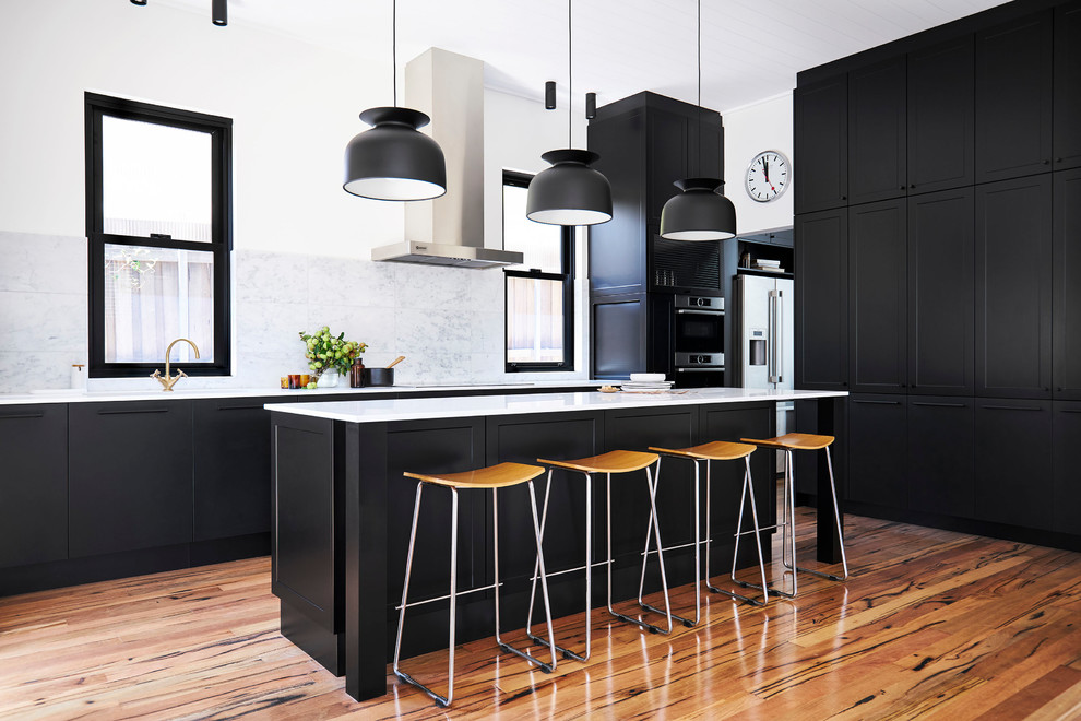 Photo of a mid-sized transitional single-wall kitchen in Sydney with black cabinets, white splashback, marble splashback, stainless steel appliances, light hardwood floors, with island and brown floor.