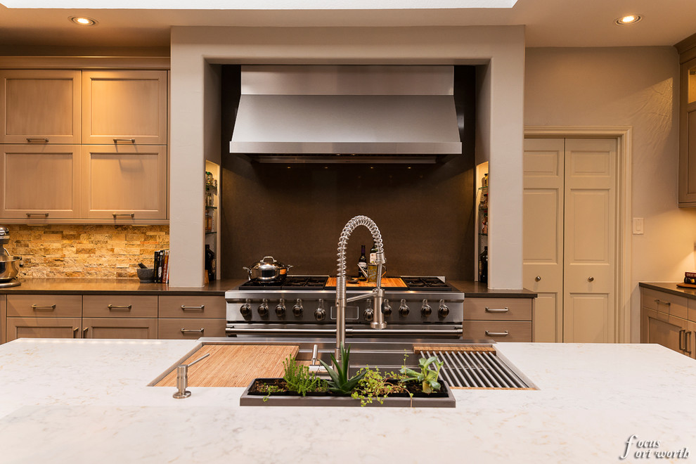 Example of a mid-sized transitional u-shaped enclosed kitchen design in Dallas with an undermount sink, flat-panel cabinets, light wood cabinets, stone tile backsplash, stainless steel appliances and an island