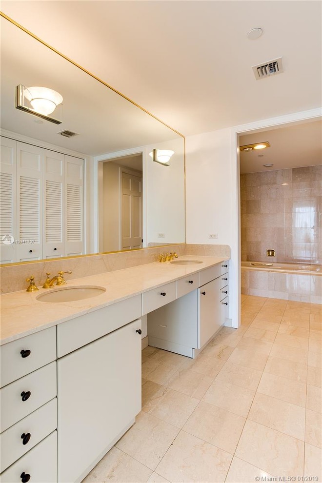 This is an example of a traditional bathroom in Miami with flat-panel cabinets, white cabinets, marble benchtops and beige benchtops.