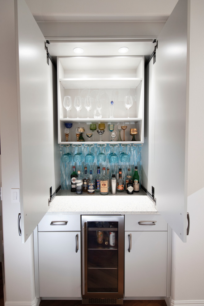 Photo of a large contemporary u-shaped home bar in San Diego with a drop-in sink, flat-panel cabinets, white cabinets, stainless steel benchtops, blue splashback, mosaic tile splashback, medium hardwood floors and white benchtop.