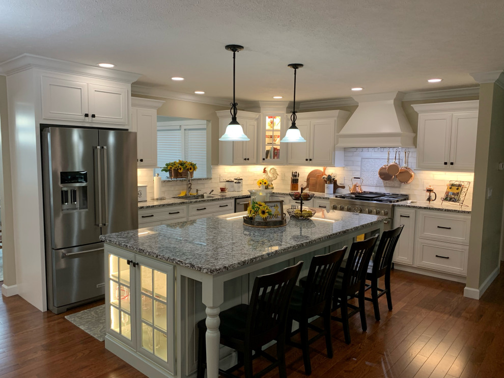 Inspiration for a transitional l-shaped medium tone wood floor and brown floor kitchen remodel with an undermount sink, recessed-panel cabinets, white cabinets, granite countertops, ceramic backsplash, stainless steel appliances, an island and gray countertops