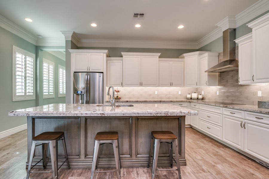 Eat-in kitchen - large transitional l-shaped medium tone wood floor and brown floor eat-in kitchen idea in Phoenix with an undermount sink, raised-panel cabinets, white cabinets, granite countertops, beige backsplash, subway tile backsplash, stainless steel appliances and an island