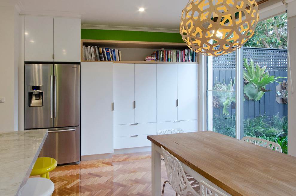Design ideas for a mid-sized contemporary l-shaped eat-in kitchen in Melbourne with an undermount sink, flat-panel cabinets, white cabinets, granite benchtops, metallic splashback, glass sheet splashback, stainless steel appliances, medium hardwood floors and with island.