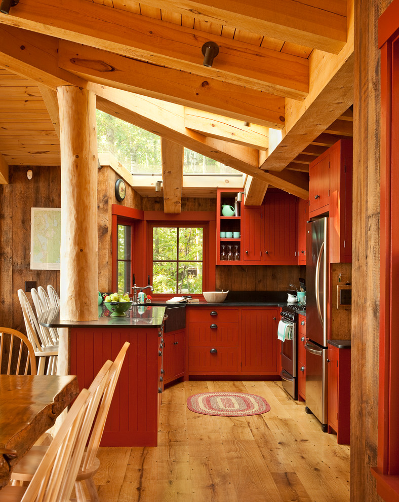 This is an example of a country u-shaped kitchen in Portland Maine with a farmhouse sink, red cabinets, soapstone benchtops, stainless steel appliances, medium hardwood floors and window splashback.