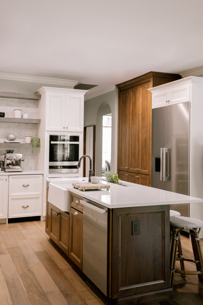 Large transitional l-shaped laminate floor and brown floor kitchen pantry photo in Orlando with a farmhouse sink, recessed-panel cabinets, white cabinets, quartz countertops, gray backsplash, black appliances, an island and white countertops