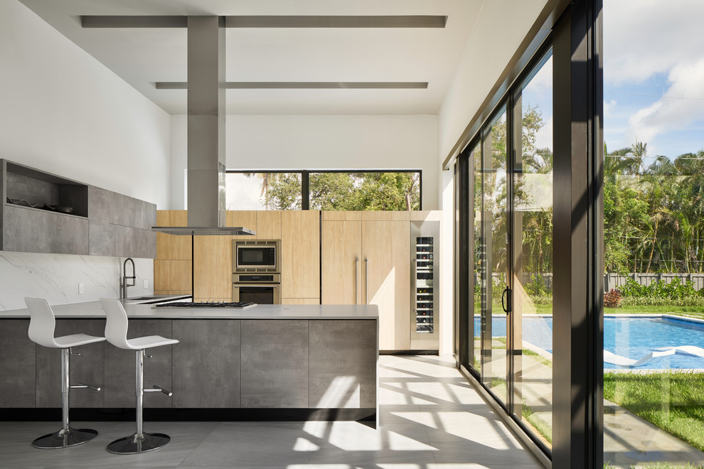 This is an example of a modern kitchen in Miami with an undermount sink, flat-panel cabinets, light wood cabinets, white splashback, panelled appliances, a peninsula and grey floor.