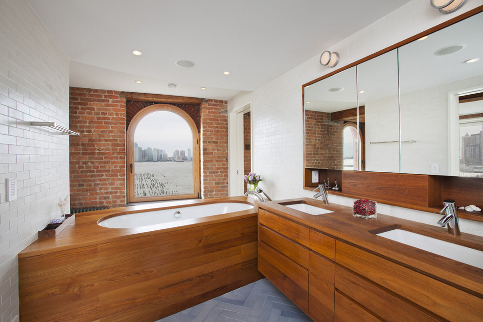Modern bathroom in New York with an undermount sink, flat-panel cabinets, medium wood cabinets, wood benchtops, an undermount tub, white tile, subway tile and brown benchtops.