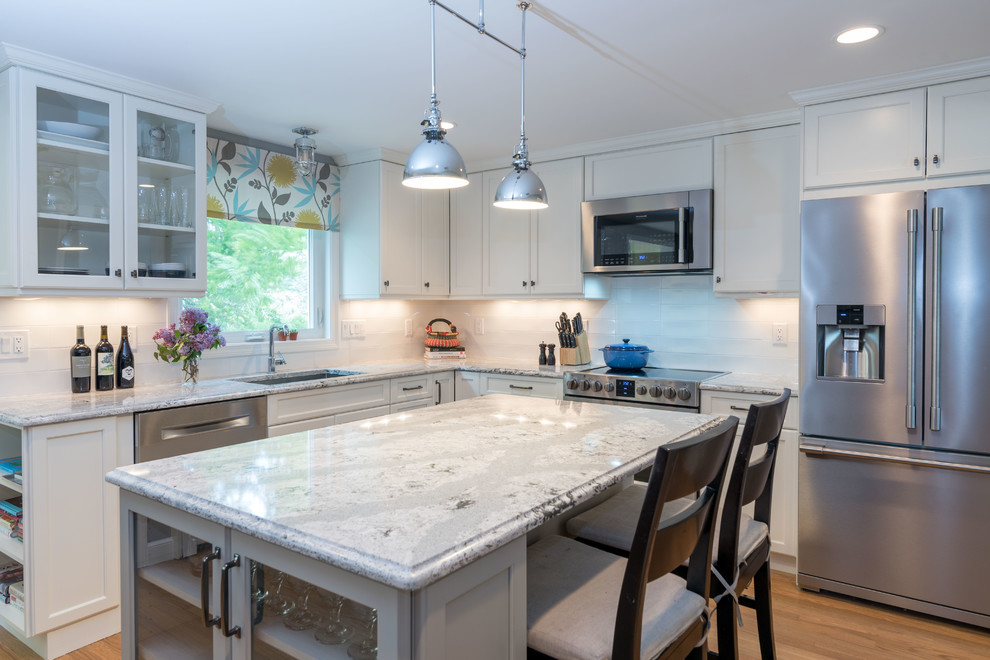 Inspiration for a mid-sized transitional l-shaped medium tone wood floor and brown floor eat-in kitchen remodel in Boston with an undermount sink, shaker cabinets, white cabinets, quartz countertops, white backsplash, ceramic backsplash, stainless steel appliances and an island