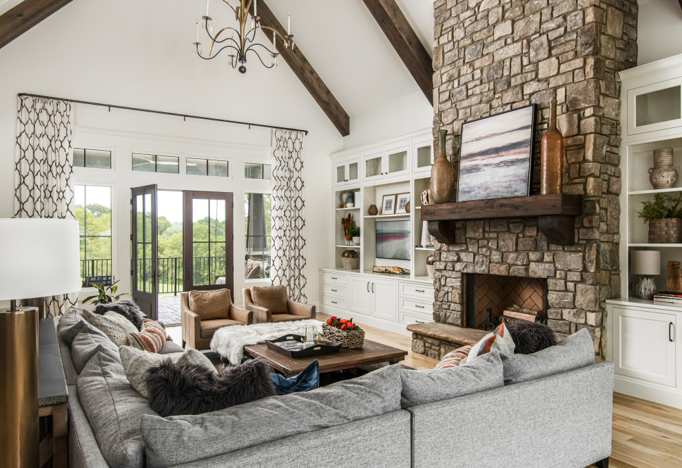 Photo of a large transitional open concept living room in Nashville with white walls, medium hardwood floors, a standard fireplace, a stone fireplace surround, a built-in media wall and vaulted.