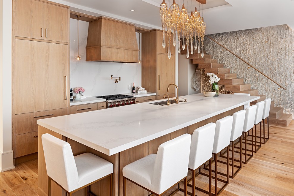 Contemporary kitchen in Toronto with a double-bowl sink, flat-panel cabinets, light wood cabinets, white splashback, stone slab splashback, stainless steel appliances, light hardwood floors, with island, beige floor and white benchtop.