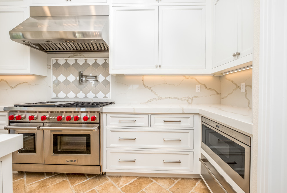 Mid-sized transitional l-shaped porcelain tile and beige floor enclosed kitchen photo in Orange County with recessed-panel cabinets, white cabinets, quartz countertops, white backsplash, marble backsplash, stainless steel appliances, an island and a farmhouse sink