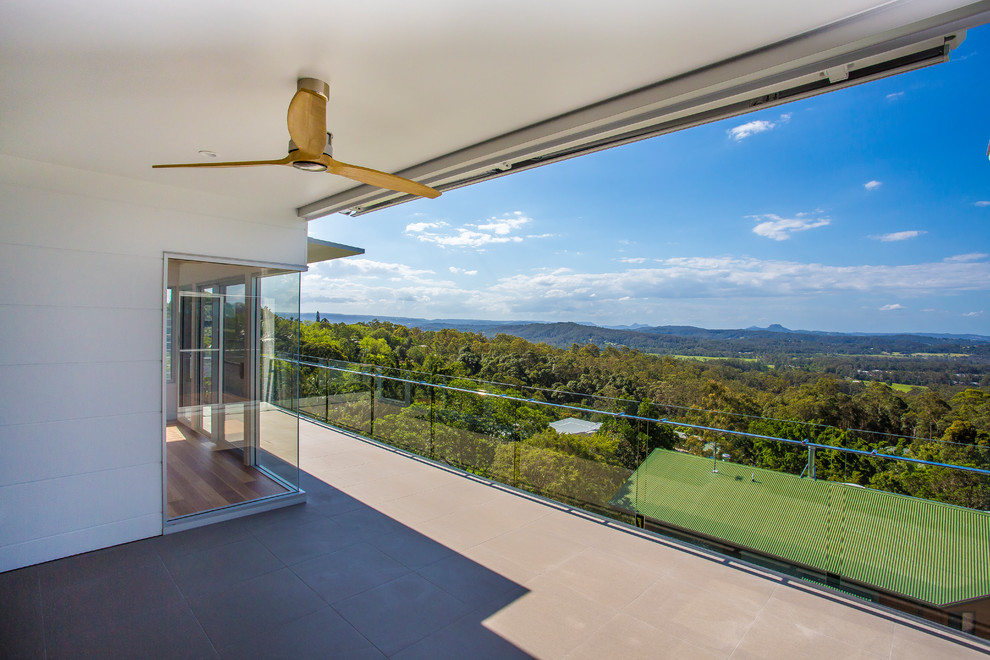 Photo of a large contemporary balcony in Sunshine Coast with a roof extension and glass railing.