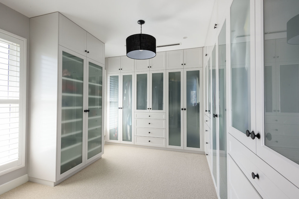 Transitional storage and wardrobe in Melbourne with glass-front cabinets, white cabinets and carpet.