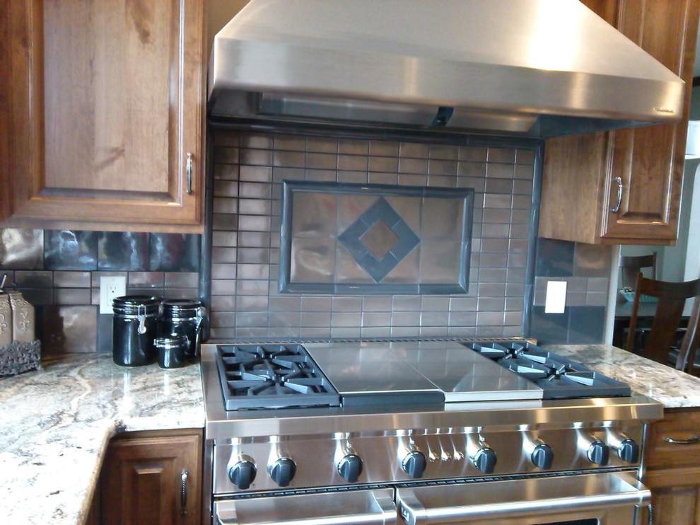 Inspiration for a rustic kitchen remodel with raised-panel cabinets, medium tone wood cabinets, granite countertops, metallic backsplash, metal backsplash and stainless steel appliances