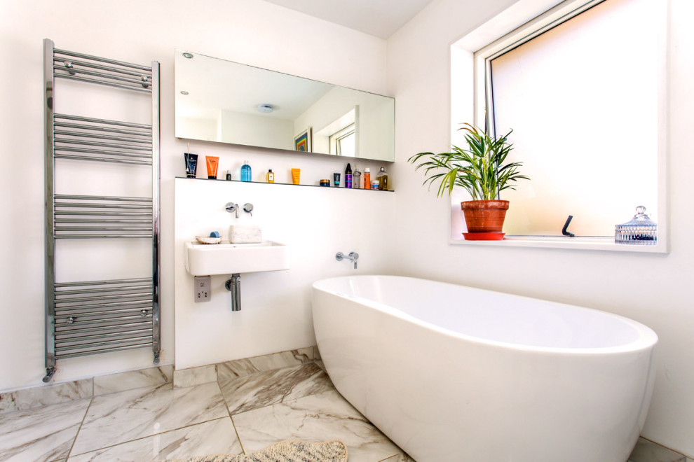 Inspiration for a mid-sized contemporary kids bathroom in Sussex with a freestanding tub, white walls, a wall-mount sink, grey floor, a single vanity, a corner shower, a wall-mount toilet, multi-coloured tile, marble floors, glass benchtops, a hinged shower door and grey benchtops.
