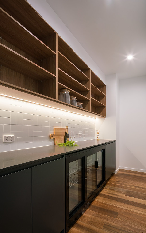 Mid-sized contemporary galley kitchen pantry in Sunshine Coast with black cabinets, quartz benchtops, white splashback, subway tile splashback, black appliances, medium hardwood floors, no island, multi-coloured floor and black benchtop.