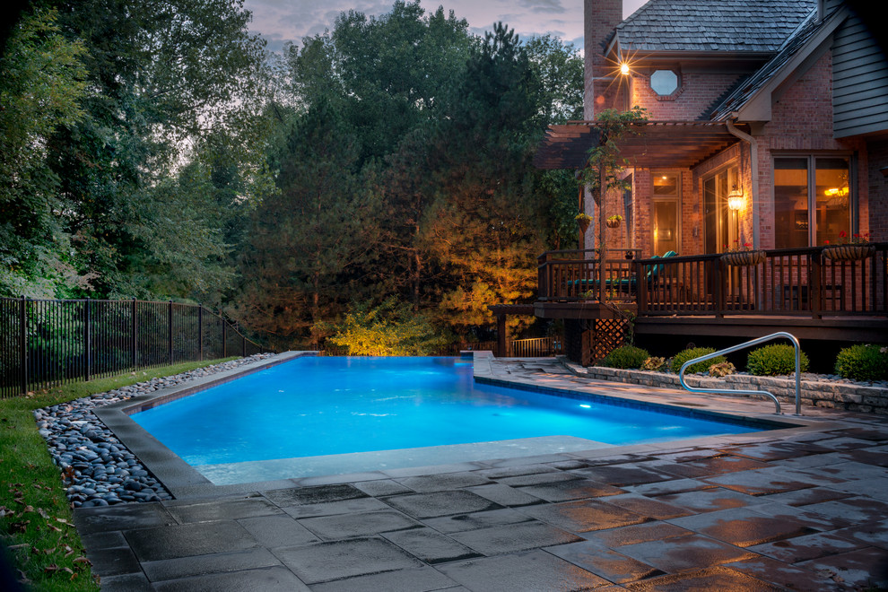 This is an example of a mid-sized country backyard l-shaped lap pool in Chicago with a water feature and natural stone pavers.