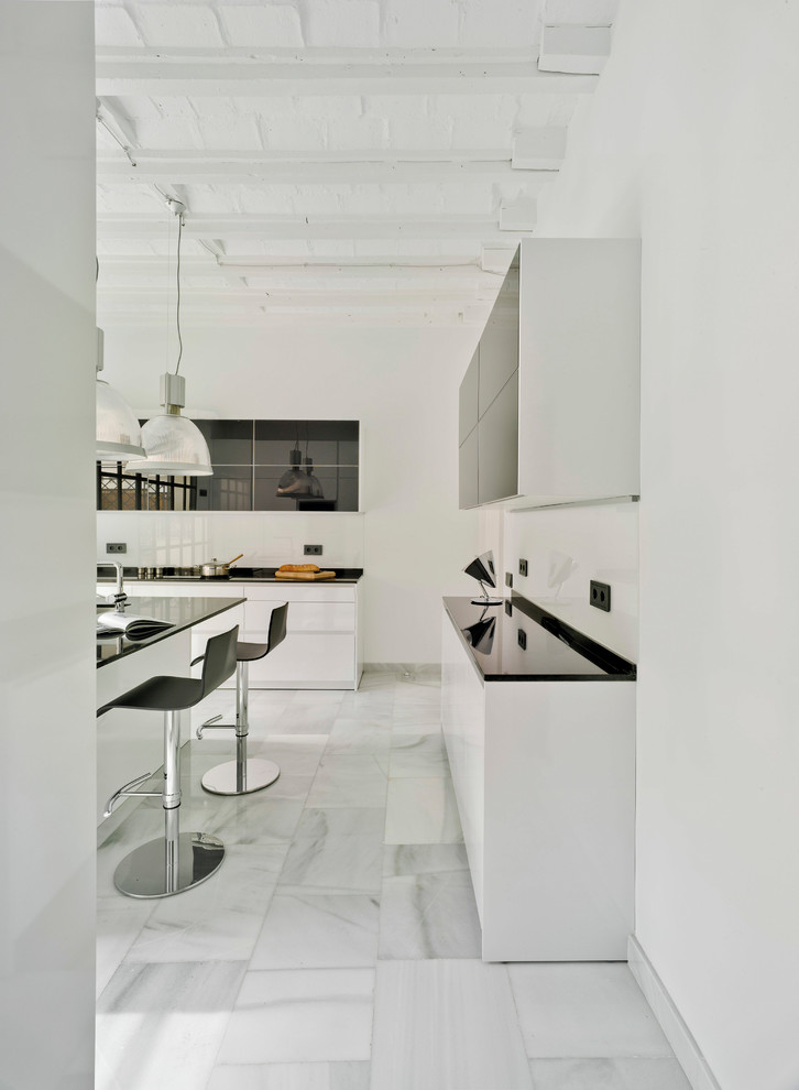 Photo of a contemporary kitchen in Madrid with an undermount sink, flat-panel cabinets, white cabinets, granite benchtops, white splashback, black appliances, with island, white floor and marble floors.