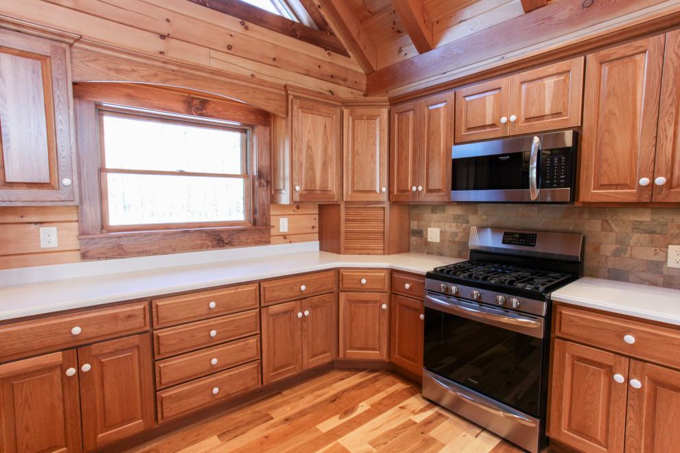 Mountain style u-shaped light wood floor, yellow floor and wood ceiling eat-in kitchen photo with a double-bowl sink, raised-panel cabinets, medium tone wood cabinets, wood backsplash, stainless steel appliances, an island and white countertops