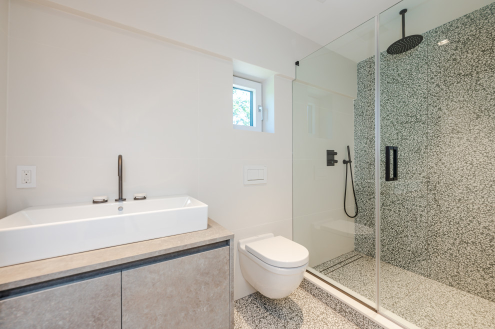 This is an example of a mid-sized modern 3/4 bathroom in New York with flat-panel cabinets, an alcove shower, a bidet, multi-coloured walls, engineered quartz benchtops, multi-coloured floor, a hinged shower door, a niche, a single vanity, a floating vanity, beige cabinets, white tile, pebble tile floors, a vessel sink and beige benchtops.