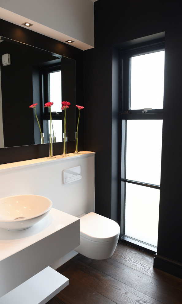 Inspiration for a small modern bathroom in Dublin with open cabinets, white cabinets, a wall-mount toilet, white tile, mirror tile, black walls, dark hardwood floors, a vessel sink, solid surface benchtops, brown floor, white benchtops, a single vanity and a built-in vanity.