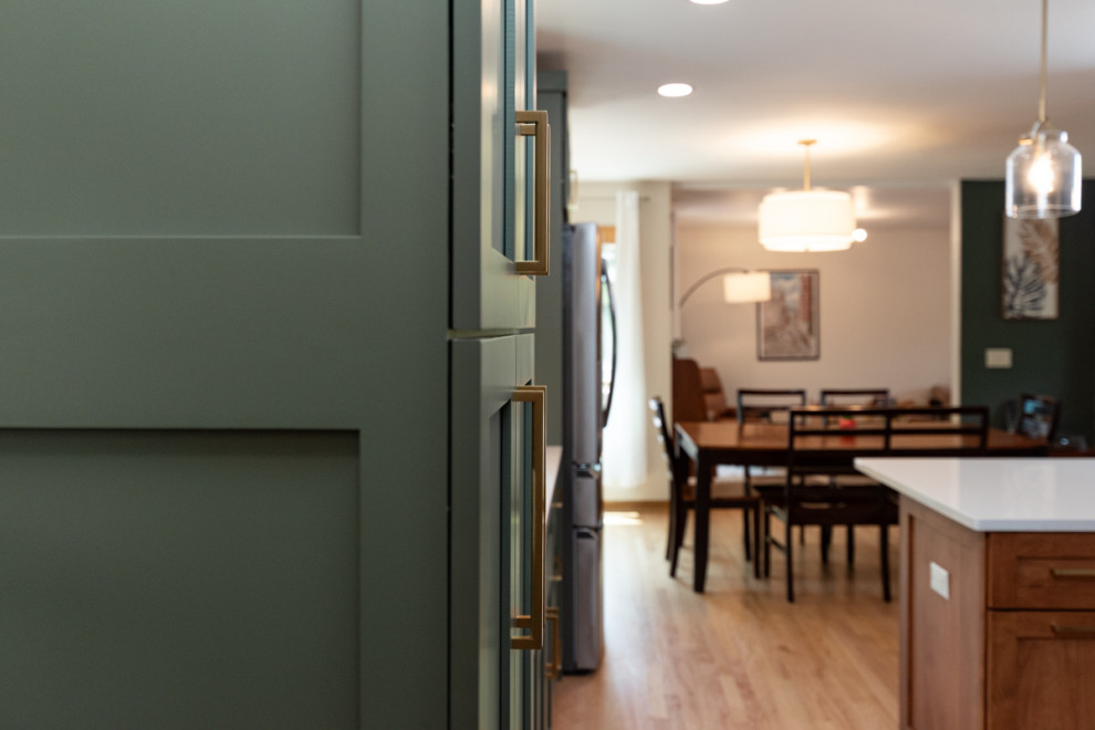 Example of a transitional light wood floor kitchen design with shaker cabinets, green cabinets, quartz countertops, white backsplash, ceramic backsplash and an island