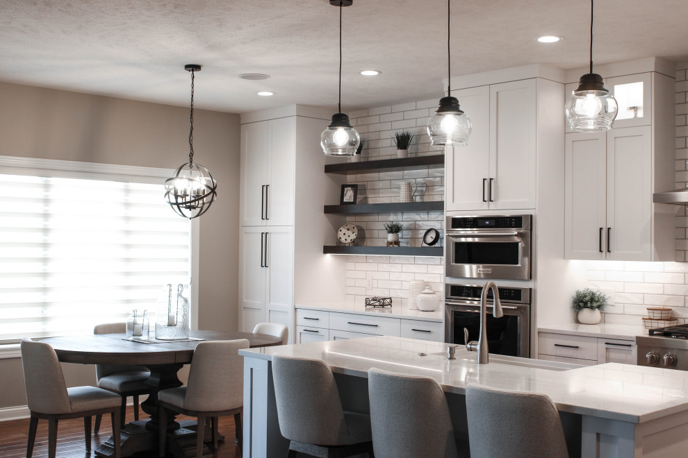 Eat-in kitchen - transitional u-shaped medium tone wood floor and brown floor eat-in kitchen idea with a farmhouse sink, shaker cabinets, white cabinets, quartz countertops, white backsplash, porcelain backsplash, stainless steel appliances, an island and white countertops