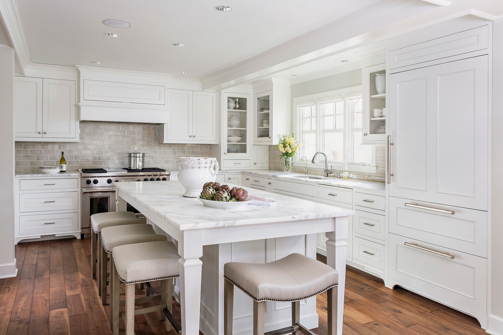 Photo of a mid-sized traditional l-shaped kitchen in Minneapolis with recessed-panel cabinets, subway tile splashback, panelled appliances, white cabinets, marble benchtops, grey splashback, an undermount sink, dark hardwood floors, with island and white benchtop.