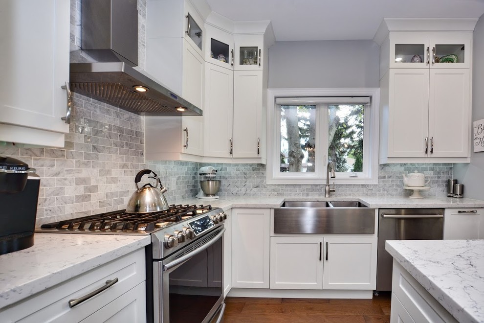 Inspiration for a mid-sized transitional l-shaped medium tone wood floor and brown floor eat-in kitchen remodel in Toronto with shaker cabinets, white cabinets, quartz countertops, gray backsplash, an island, white countertops, a farmhouse sink, marble backsplash and stainless steel appliances