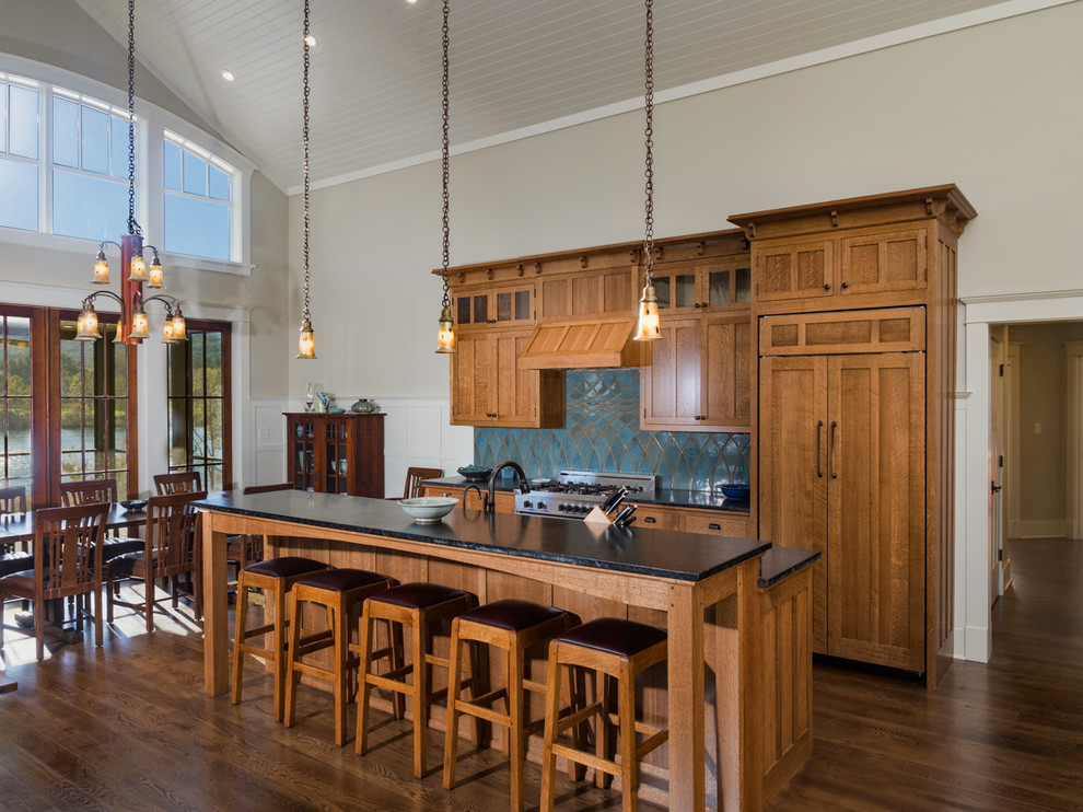 Mountain style dark wood floor and brown floor eat-in kitchen photo with medium tone wood cabinets, blue backsplash, paneled appliances, an island and black countertops
