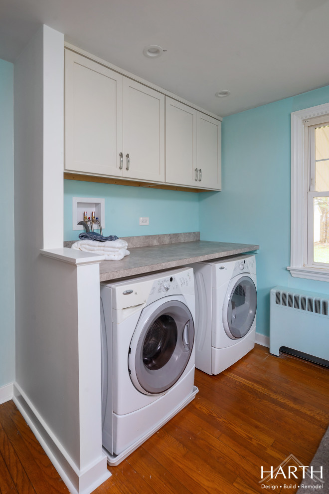 Photo of a small transitional single-wall utility room in Philadelphia with shaker cabinets, medium wood cabinets, laminate benchtops, beige splashback, blue walls, medium hardwood floors, a side-by-side washer and dryer, brown floor and beige benchtop.