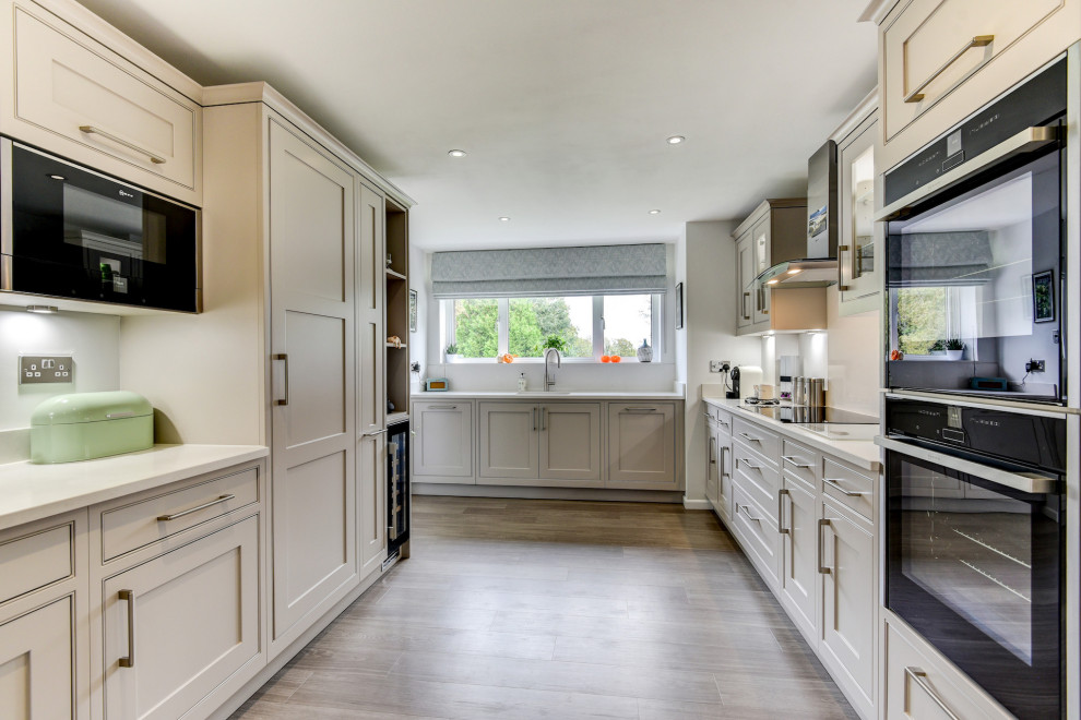 Design ideas for a large traditional galley separate kitchen in Sussex with an undermount sink, shaker cabinets, beige cabinets, quartzite benchtops, white splashback, black appliances, vinyl floors, no island, brown floor and white benchtop.