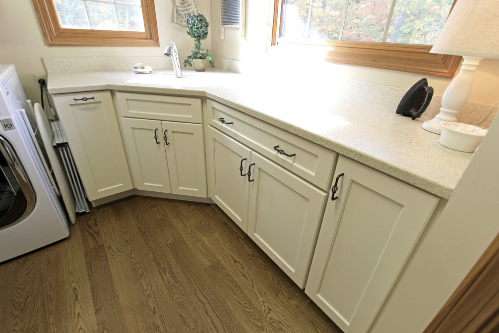 Photo of a mid-sized traditional l-shaped dedicated laundry room in Cleveland with an utility sink, flat-panel cabinets, dark wood cabinets, solid surface benchtops, beige walls, medium hardwood floors and a side-by-side washer and dryer.