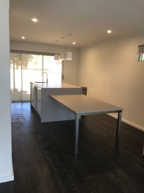 Photo of a mid-sized contemporary single-wall eat-in kitchen in Perth with an integrated sink, flat-panel cabinets, white cabinets, solid surface benchtops, dark hardwood floors and with island.