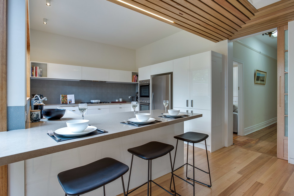 Design ideas for a large modern u-shaped eat-in kitchen in Melbourne with an undermount sink, open cabinets, white cabinets, solid surface benchtops, grey splashback, porcelain splashback, stainless steel appliances and with island.