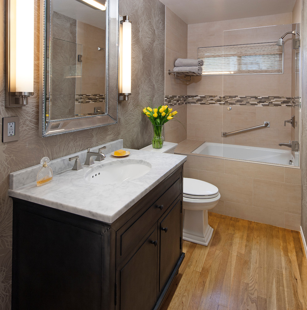 This is an example of a transitional bathroom in Santa Barbara with an undermount sink, dark wood cabinets, marble benchtops, an alcove tub, a shower/bathtub combo, a two-piece toilet, beige tile, grey walls and medium hardwood floors.