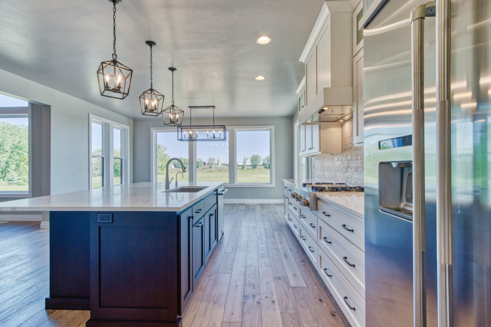 Large transitional l-shaped light wood floor and brown floor eat-in kitchen photo with an undermount sink, shaker cabinets, white cabinets, quartz countertops, white backsplash, ceramic backsplash, stainless steel appliances, an island and white countertops