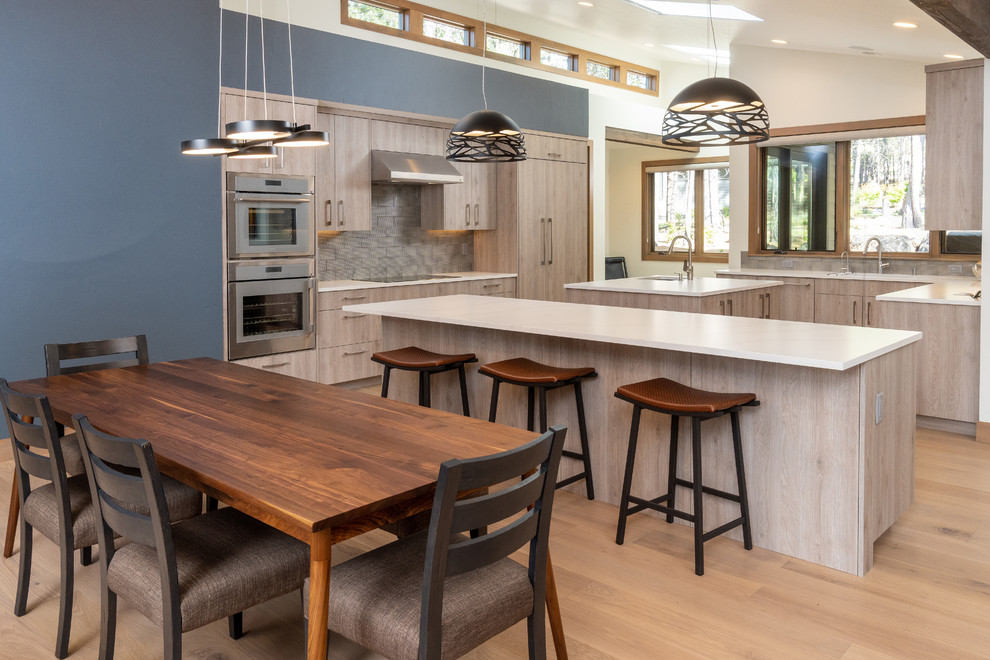 Eat-in kitchen - large rustic light wood floor and beige floor eat-in kitchen idea with an undermount sink, flat-panel cabinets, light wood cabinets, quartz countertops, gray backsplash, ceramic backsplash, paneled appliances, two islands and white countertops