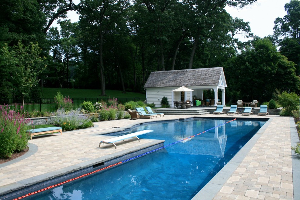 Expansive transitional backyard l-shaped lap pool in New York with a pool house and concrete pavers.