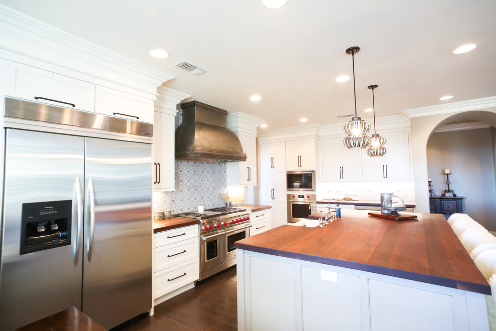 Photo of a large modern l-shaped eat-in kitchen in San Diego with a farmhouse sink, shaker cabinets, white cabinets, wood benchtops, blue splashback, cement tile splashback, stainless steel appliances, dark hardwood floors, with island, brown floor and brown benchtop.