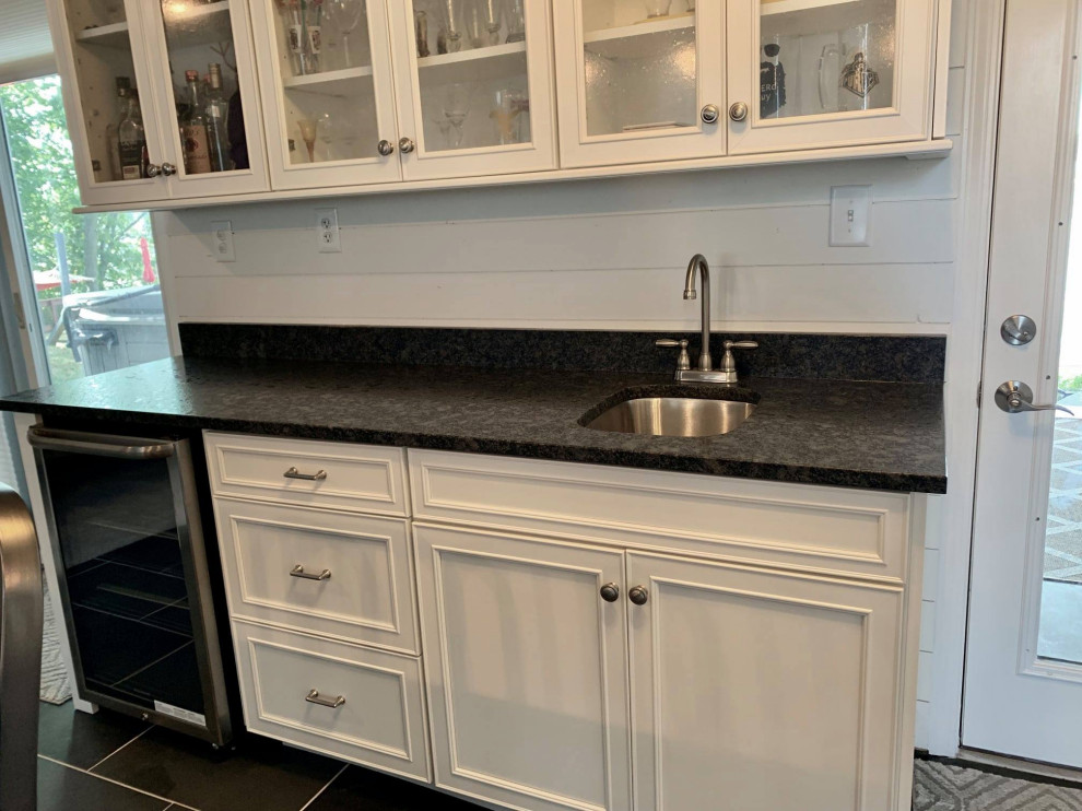 This is an example of a small contemporary galley wet bar in Indianapolis with recessed-panel cabinets, white cabinets, granite benchtops, ceramic floors, black floor and black benchtop.