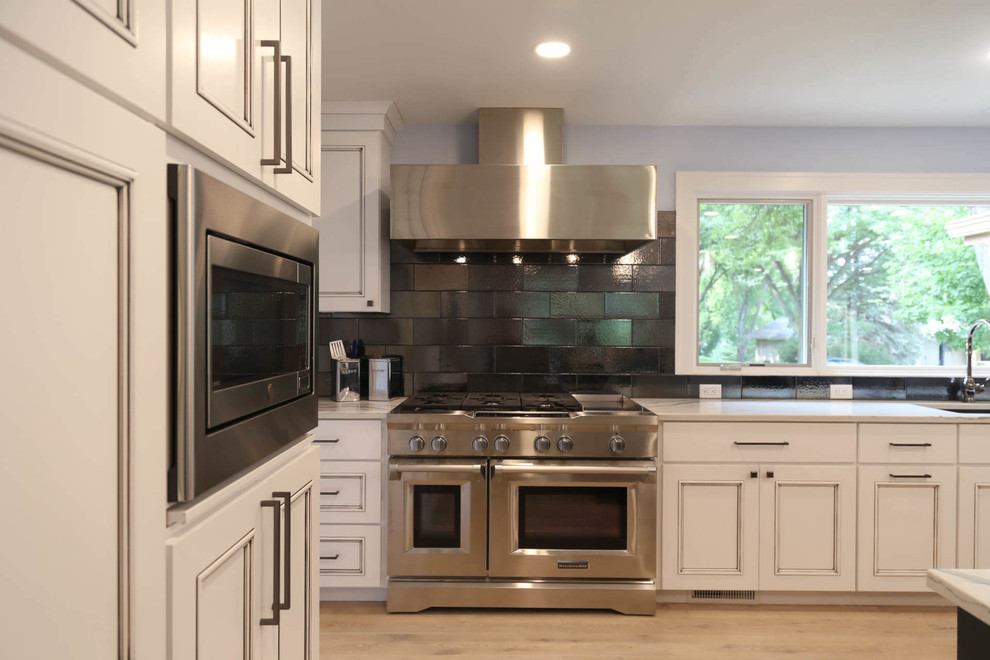 Example of a mid-sized transitional u-shaped light wood floor and beige floor eat-in kitchen design with an undermount sink, recessed-panel cabinets, white cabinets, quartzite countertops, black backsplash, porcelain backsplash, stainless steel appliances, an island and white countertops