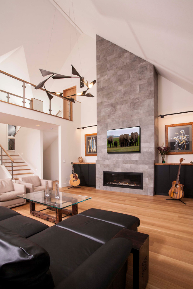 Cette photo montre un grand salon tendance ouvert avec un mur blanc, un sol en bois brun, une cheminée standard, un manteau de cheminée en carrelage, un téléviseur fixé au mur, un sol blanc et un plafond voûté.